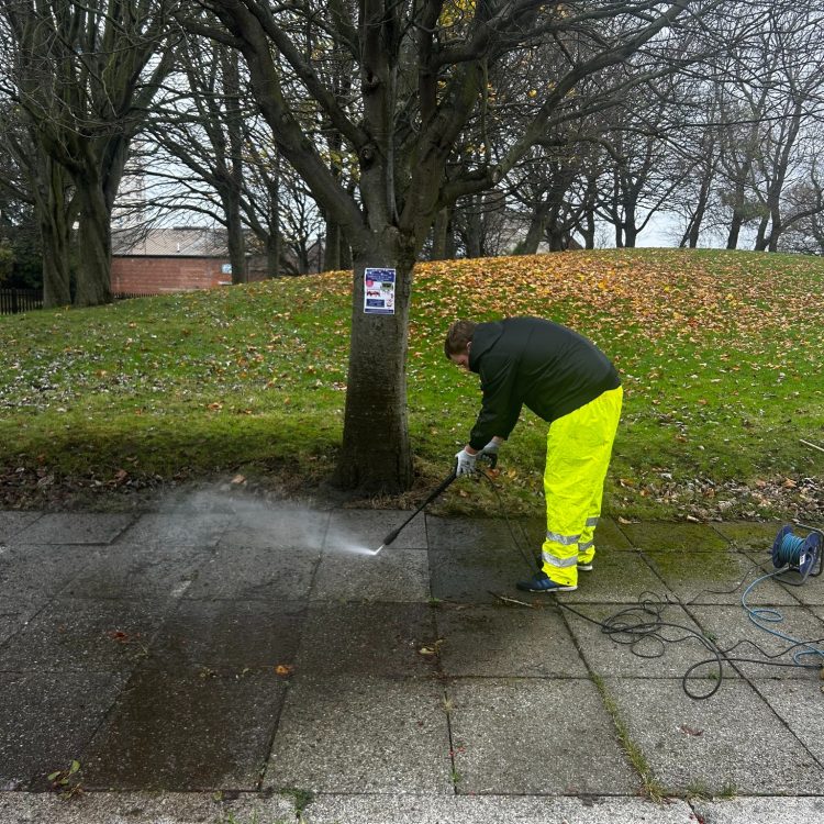 A workman from AESC power washing path